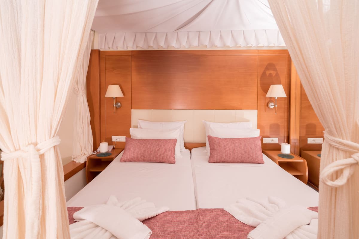 Un lit double avec une literie blanche et rose, deux tables de chevet avec des lampes et une tête de lit en bois.