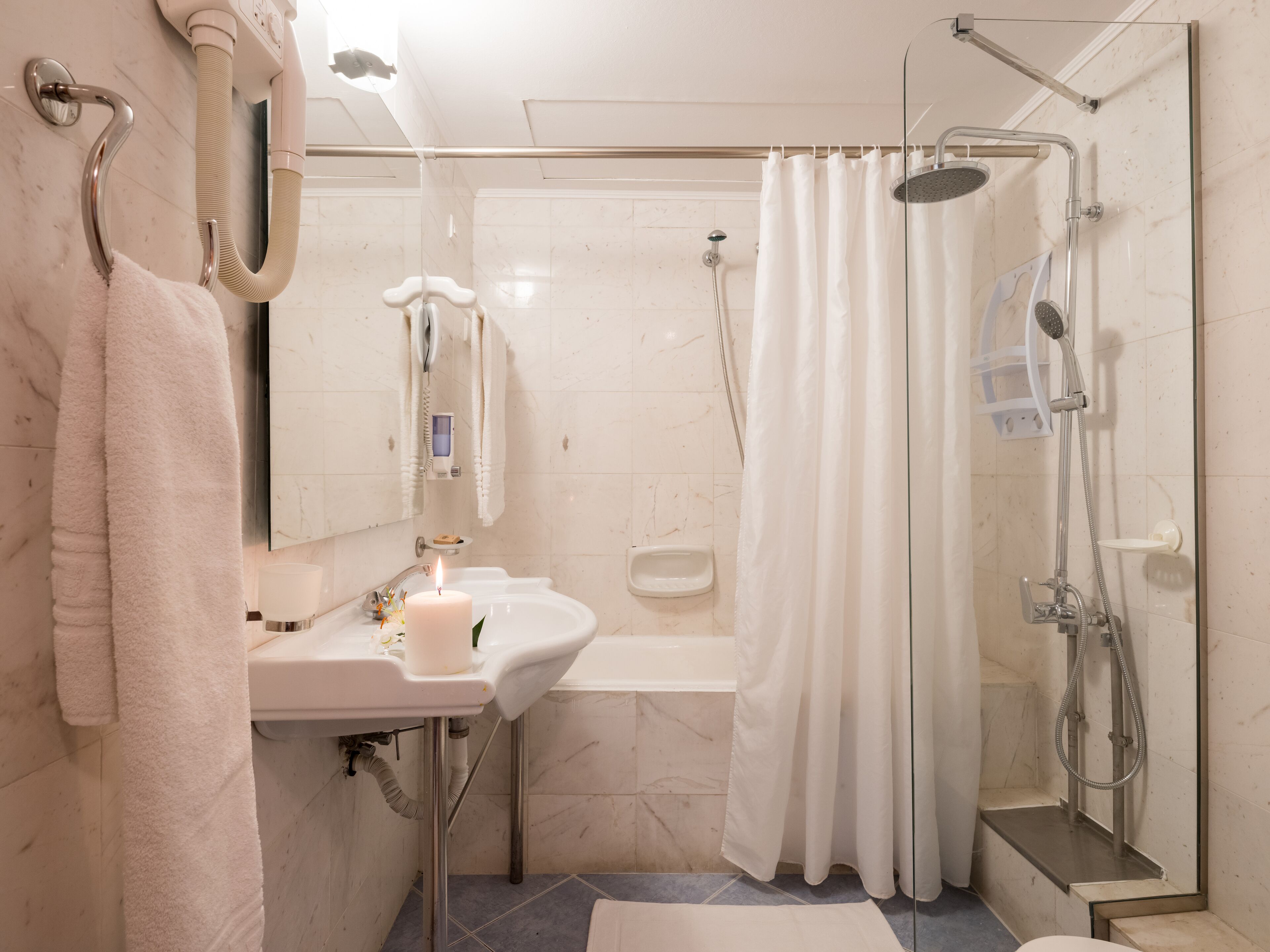 Une salle de bain équipée d’un lavabo, d’un miroir, d’un porte-serviettes, d’une douche et d’un espace de douche clos par des parois en verre.