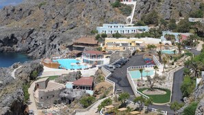 A coastal resort with multiple buildings, a swimming pool, and a rocky landscape.
