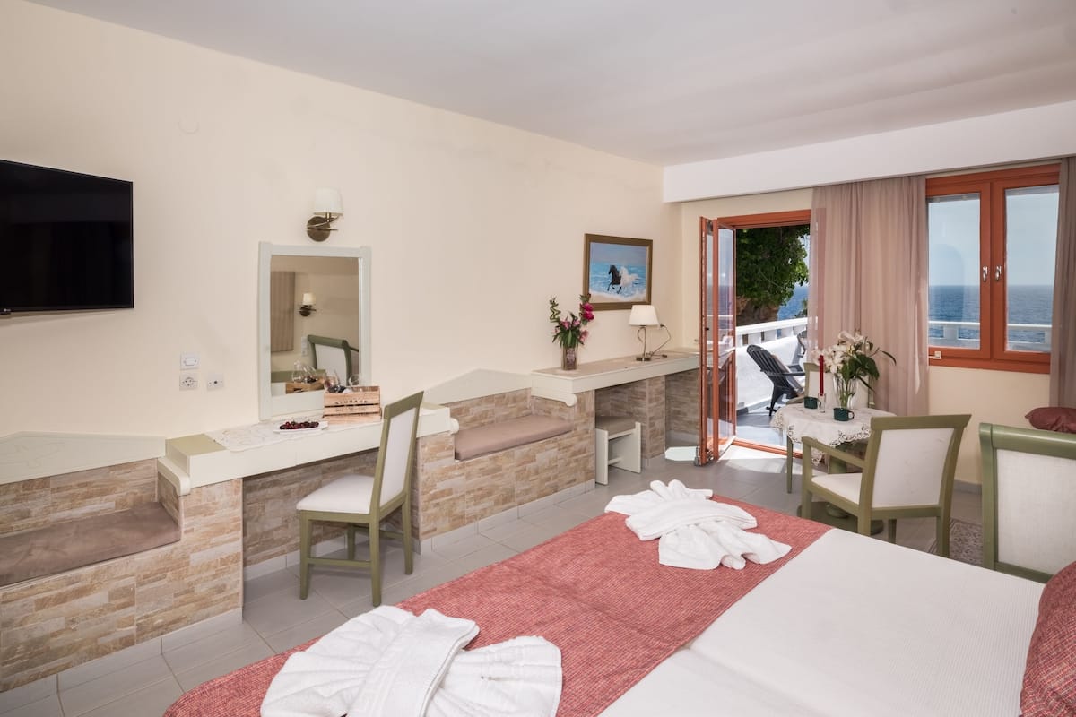 Une chambre d’hôtel comprenant un lit, un bureau, une chaise, une télévision et un balcon avec vue sur la mer.