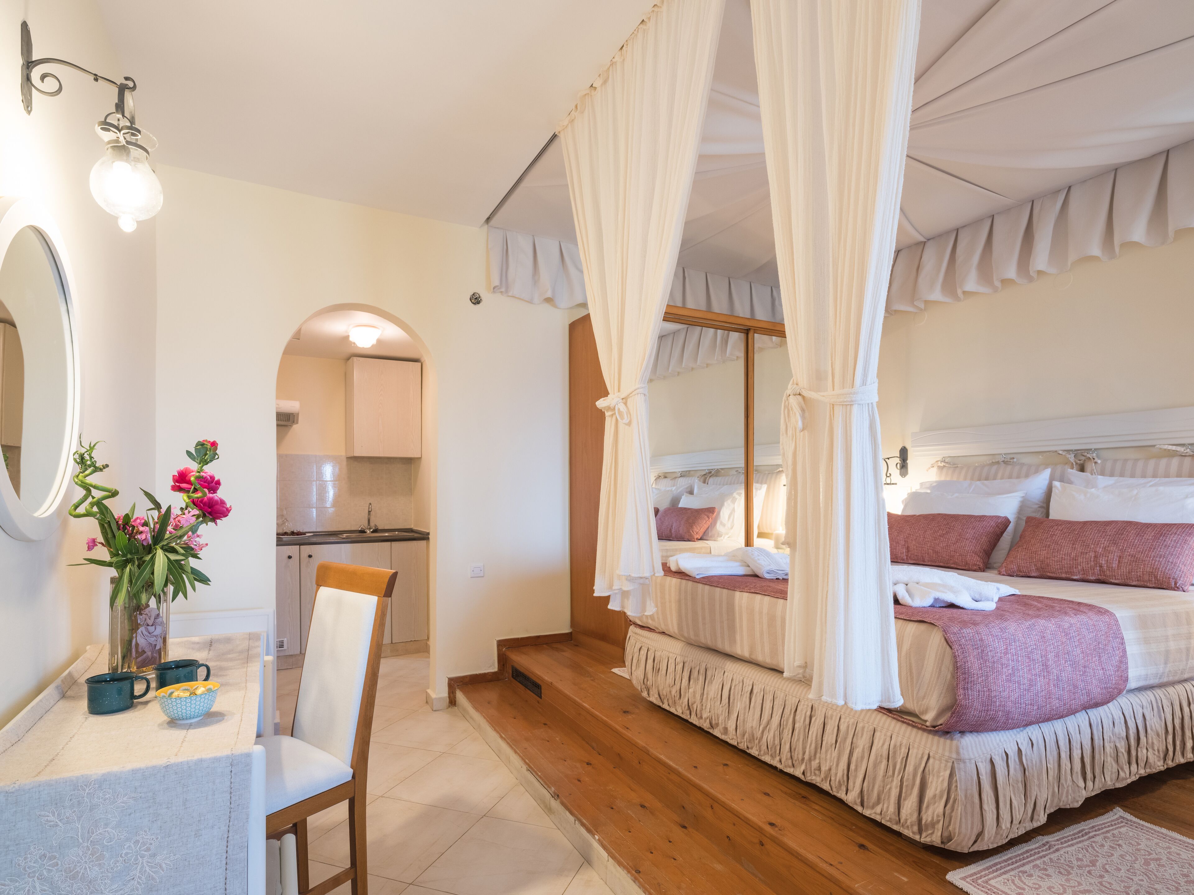 A bedroom with a canopy bed, a bedside table with a mirror, and a vase of flowers.