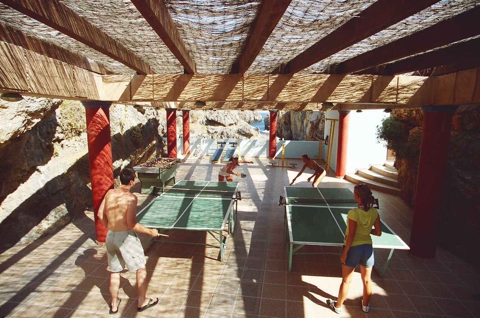 An outdoor area with multiple ping pong tables, a pool table, and a seating area with benches.