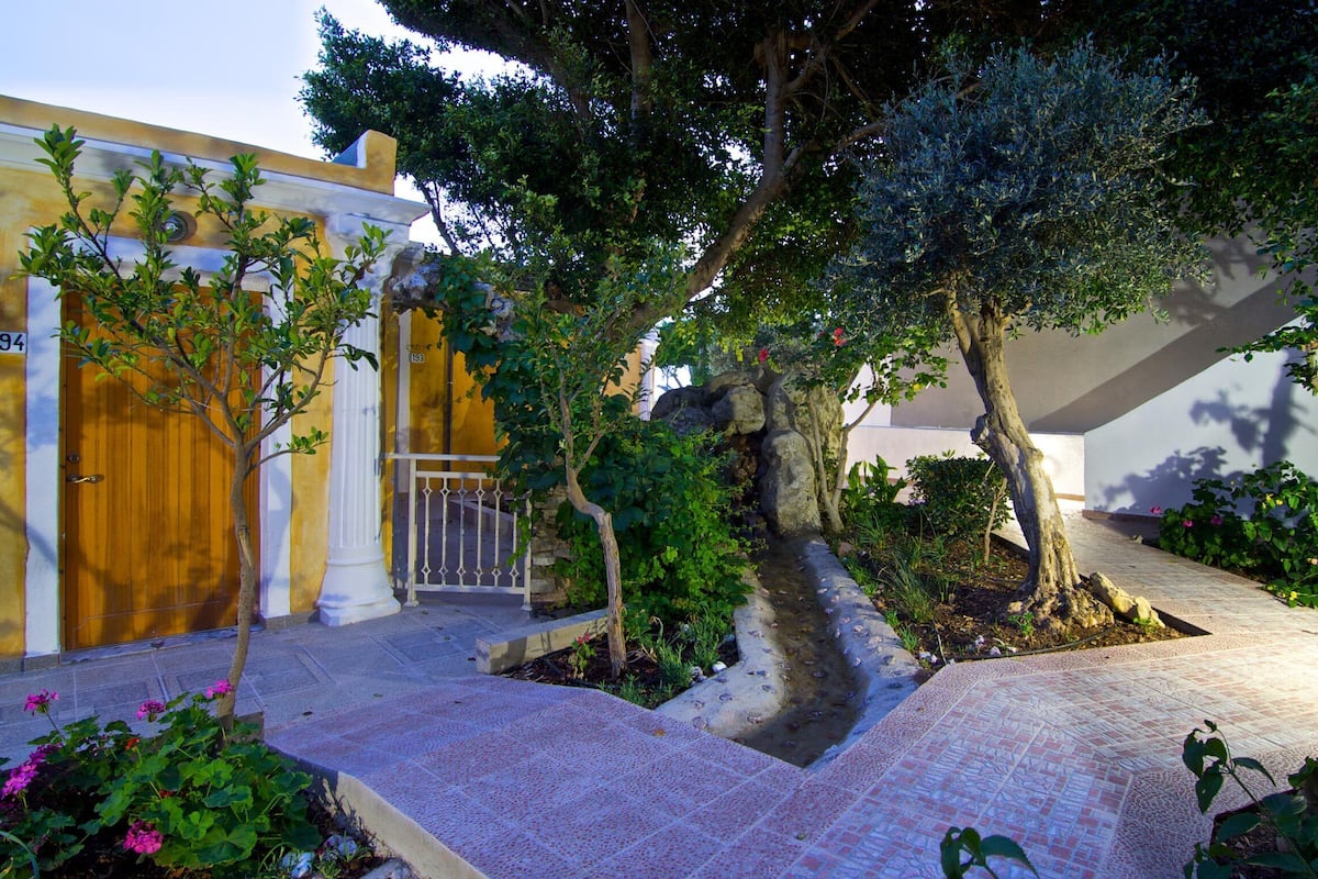 Une cour avec une porte en bois, une colonne blanche et un arbre à l’écorce épaisse.