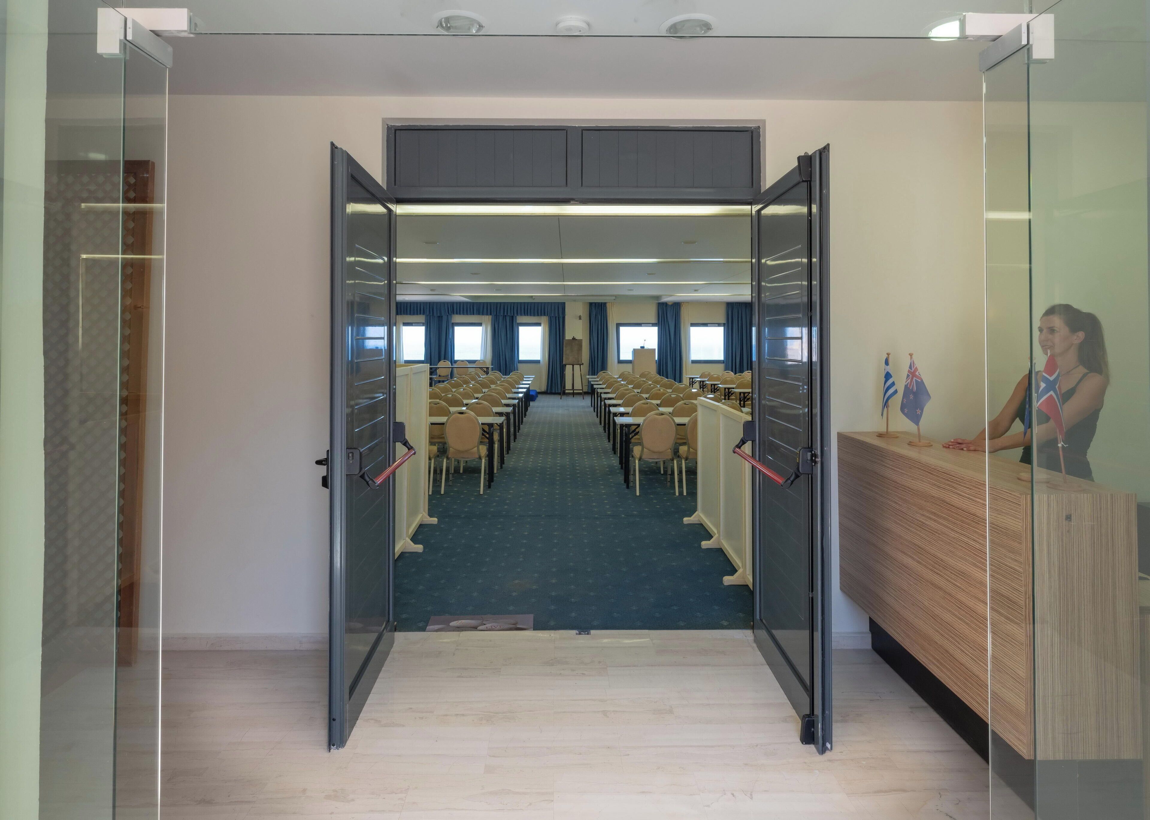 A conference room with glass walls, rows of chairs, a wooden reception desk, and flags.