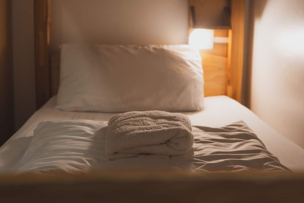 A single bed with a neatly folded white towel and a white pillow.