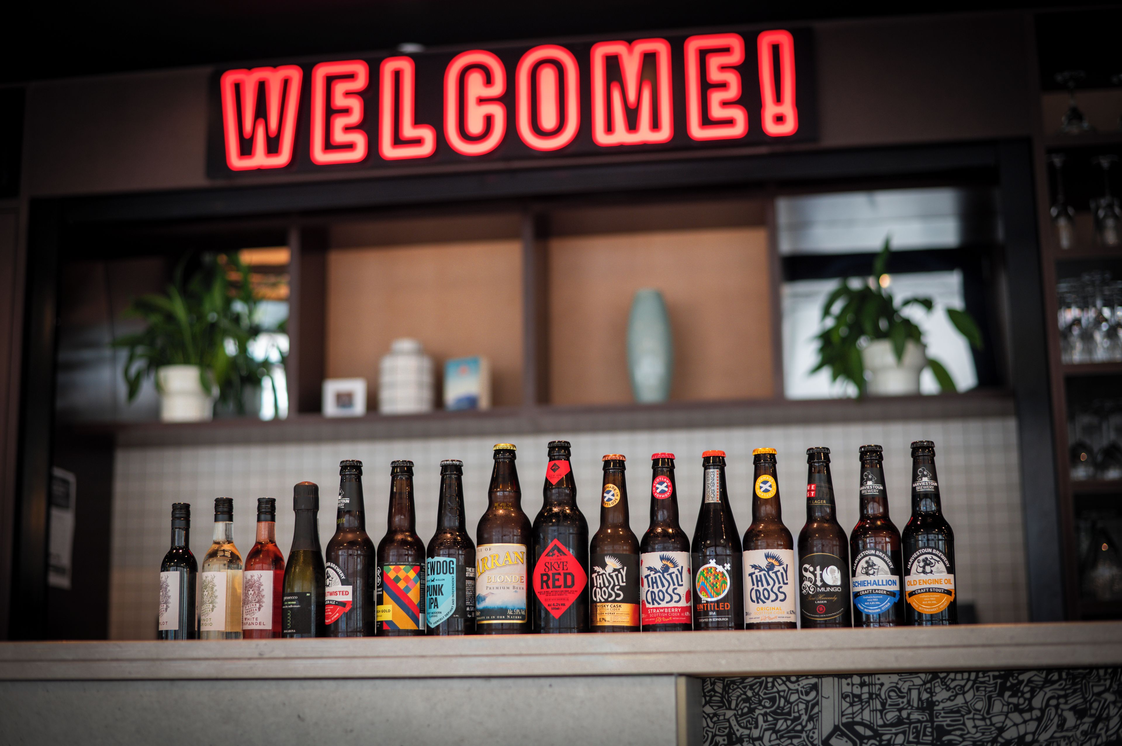 A bar with a 'WELCOME!' sign and a row of beer bottles.