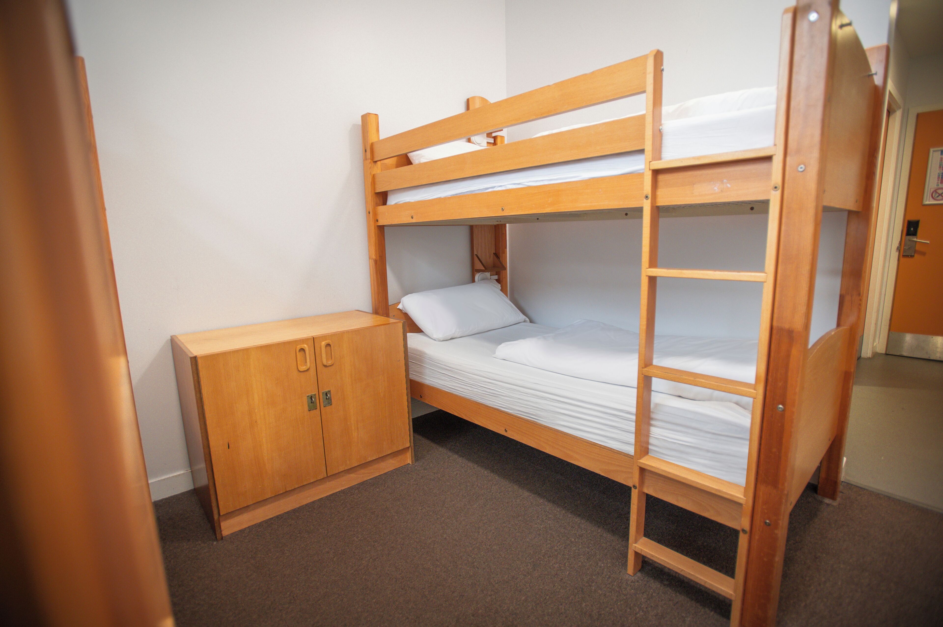 A bunk bed with a wooden ladder, a small wooden cabinet, and a door with a lock.