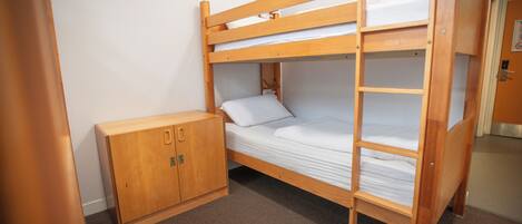 A bunk bed with a wooden ladder, a small wooden cabinet, and a door with a lock.