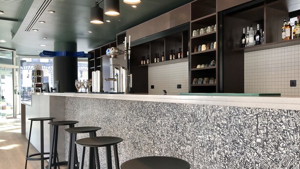 Un espace bar avec des tabourets, des étagères remplies de bouteilles et un mur décoré de motifs.