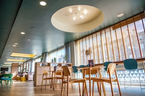 A modern interior with wooden furniture, a central light fixture, and large windows. - Edinburgh Central Youth Hostel (Edinburgh)