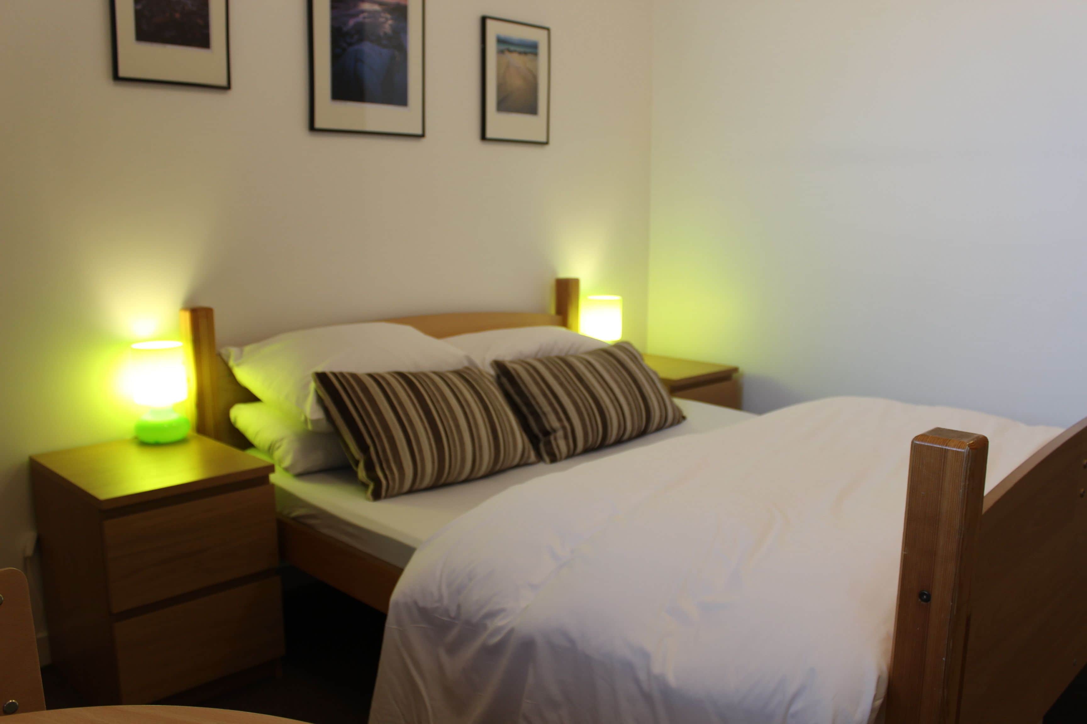 A neatly made bed with striped pillows, a wooden headboard, and two bedside lamps.