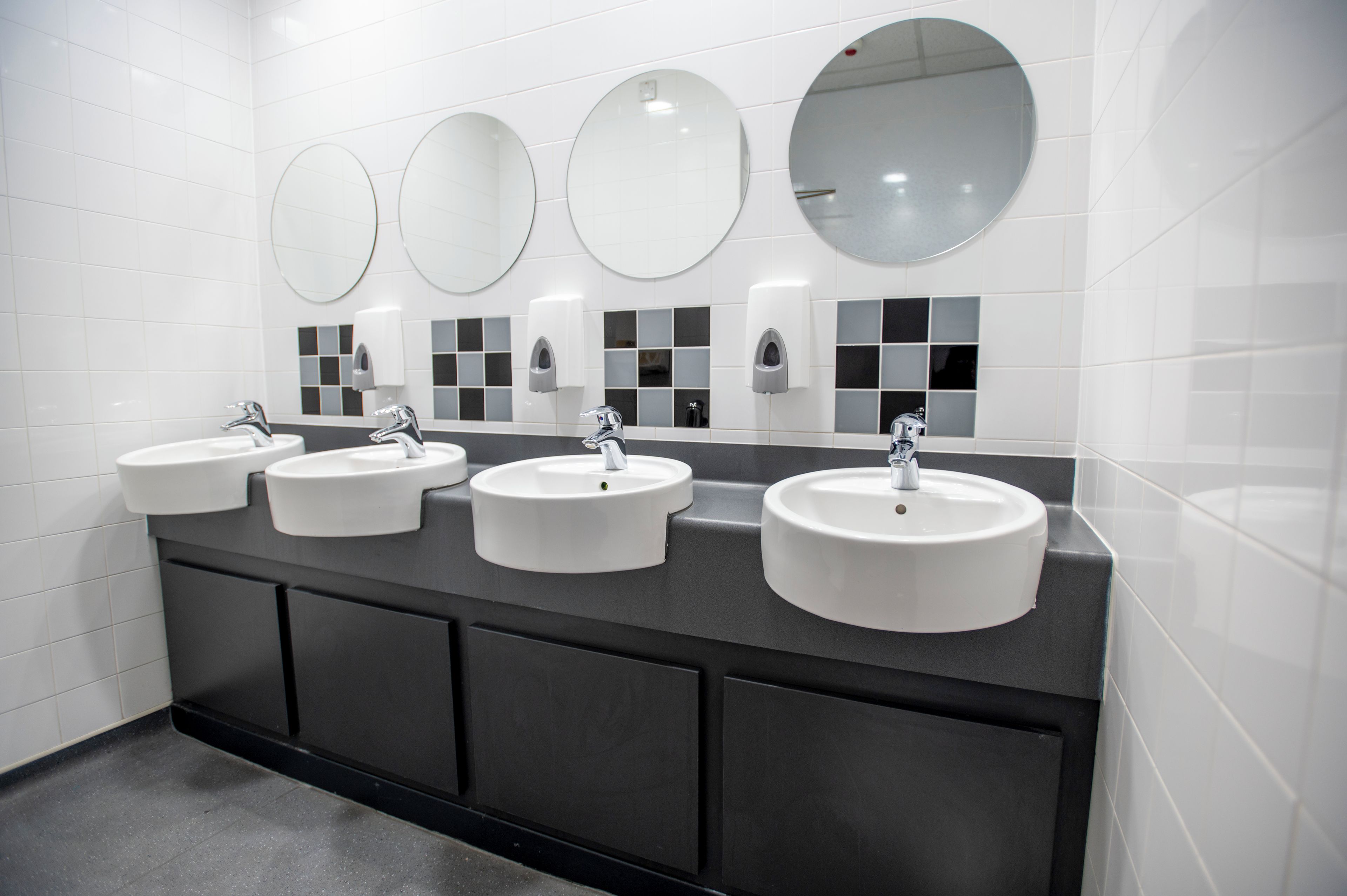 Un baño moderno con cuatro lavamanos, cada uno con espejo.