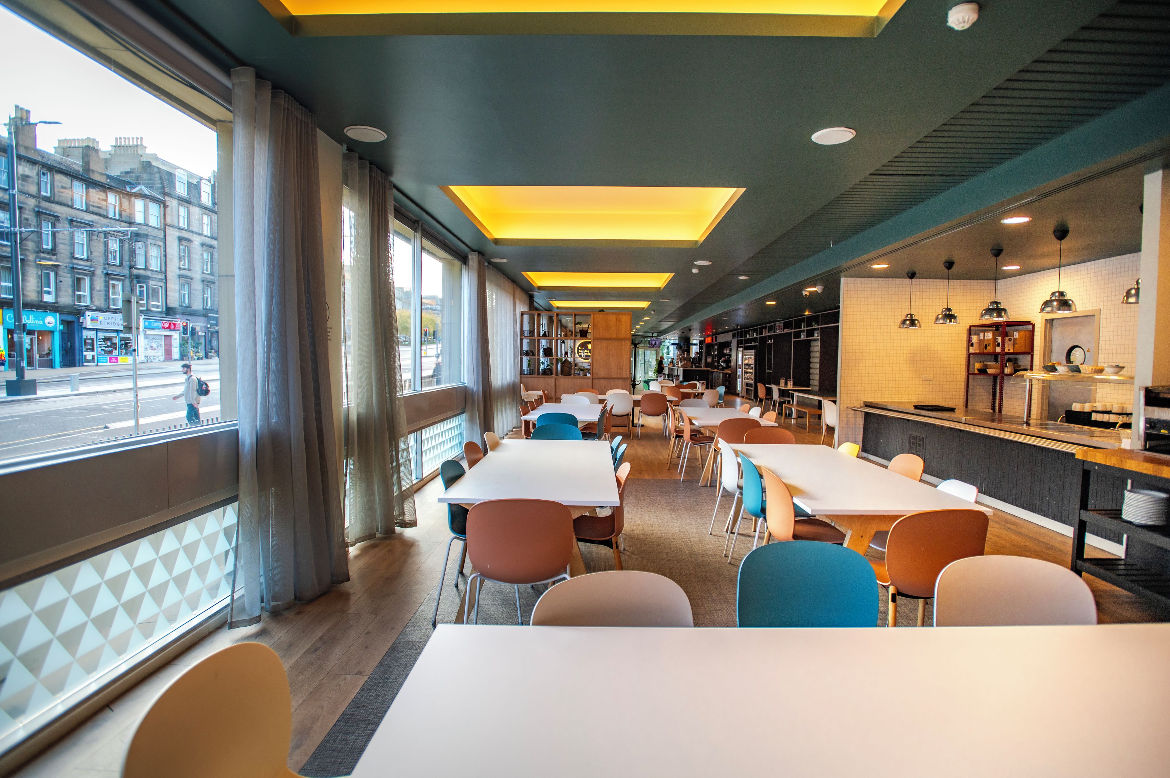 Ein modernes Restaurant mit langen Tischen, Stühlen und einem Küchenbereich.