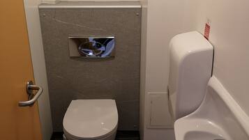 A small, compact bathroom with a toilet, urinal, and a paper towel dispenser.