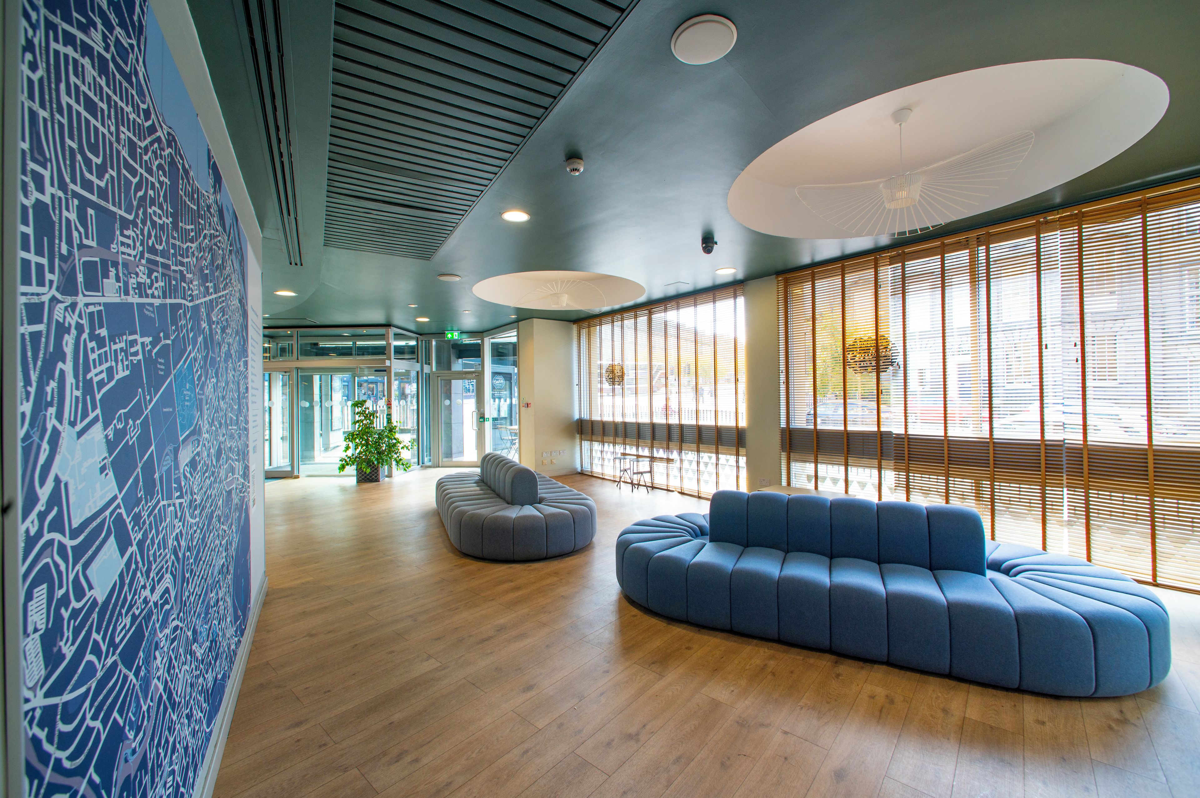 Un intérieur moderne avec un canapé bleu, un plancher en bois et de grandes fenêtres équipées de stores.