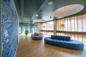 A modern interior with a blue sofa, wooden flooring, and large windows with blinds. - Edinburgh Central Youth Hostel (Edinburgh)