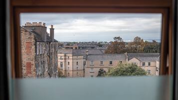 En vy genom ett fönster som visar en stadsbild med flera byggnader, inklusive en blandning av bostadshus och eventuellt även kommersiella byggnader.