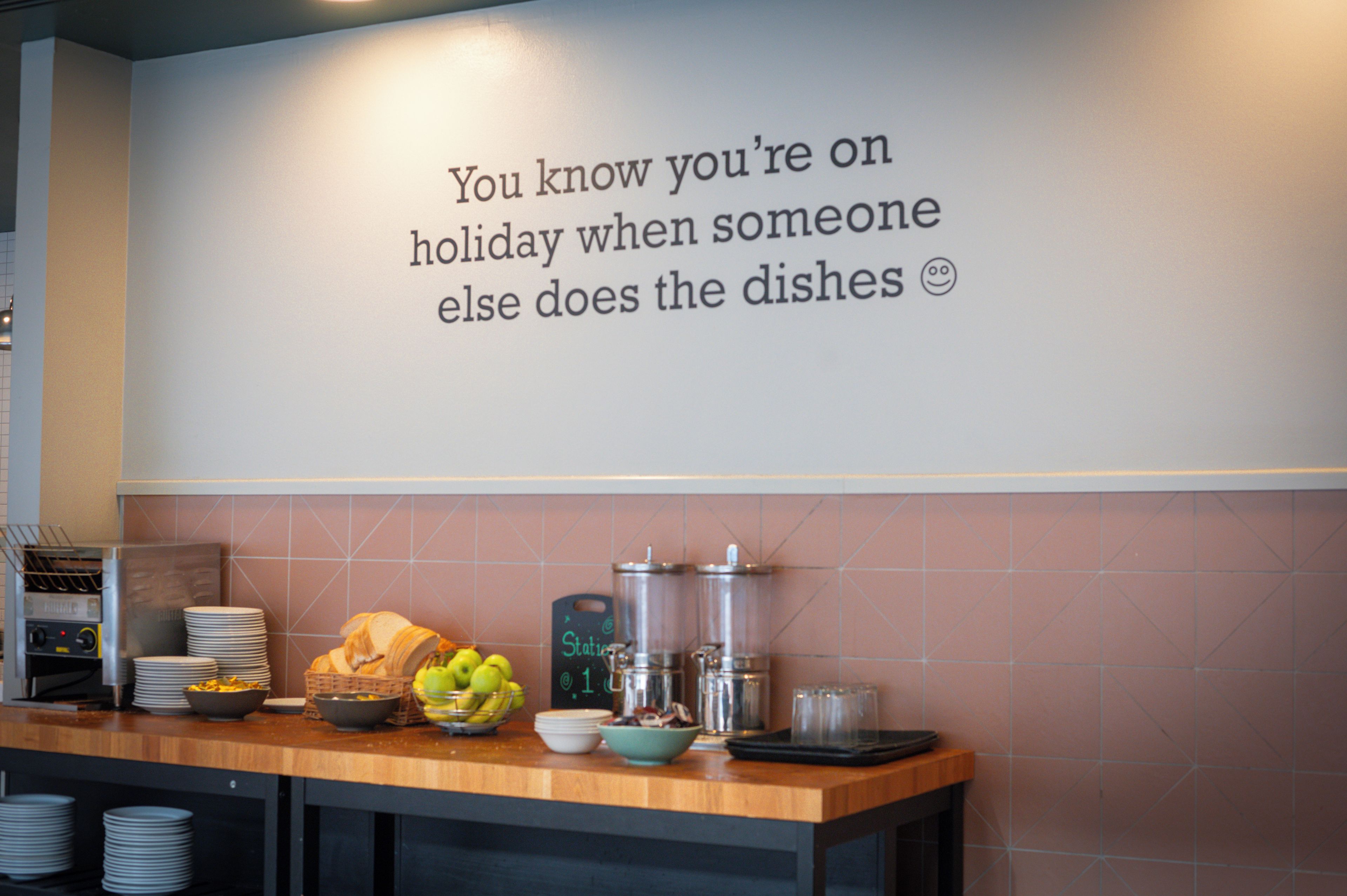 A kitchen counter with a wall sign, a fruit bowl, a coffee maker, and stacked plates.