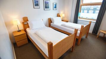 A hotel room with two wooden beds, a nightstand with a lamp, and a window with curtains.