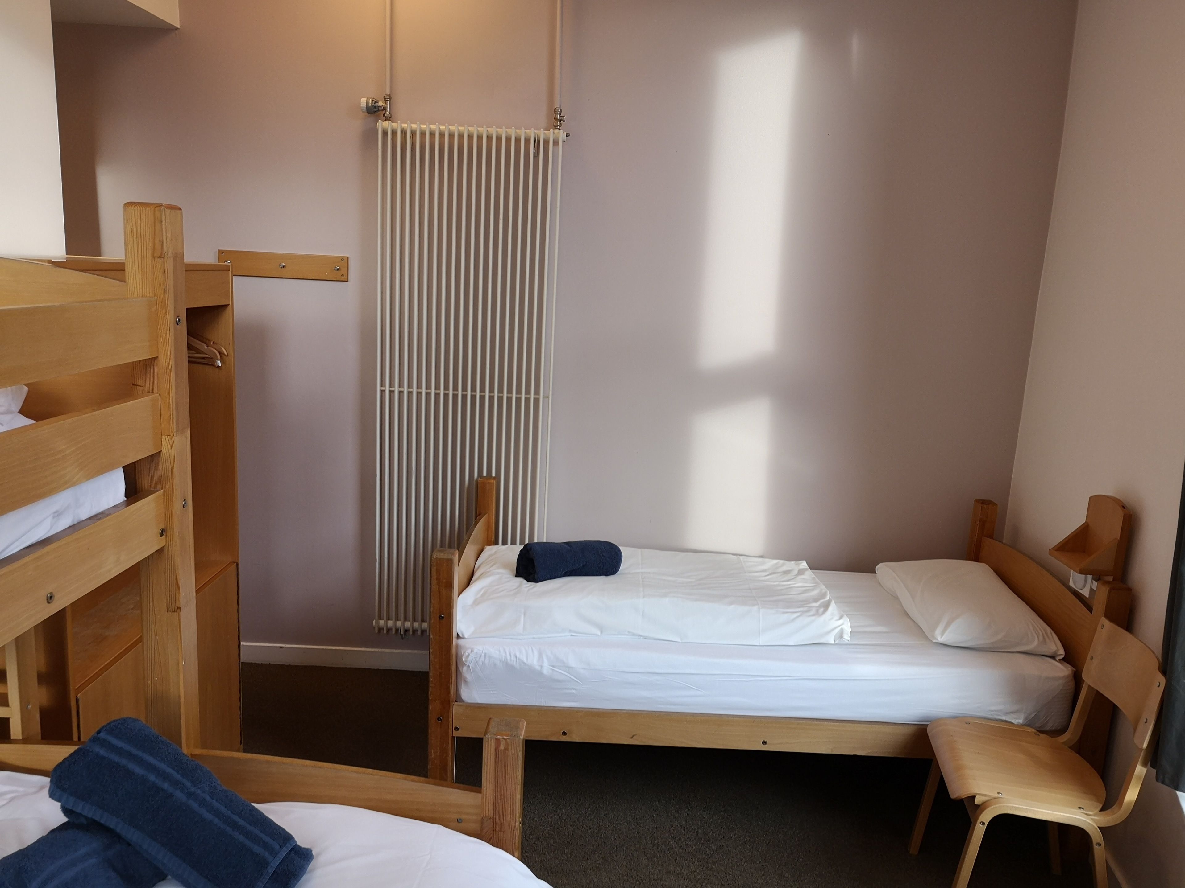 Un petit logement composé d’une seule pièce, comprenant un lit superposé, un lit simple, une chaise et un radiateur.
