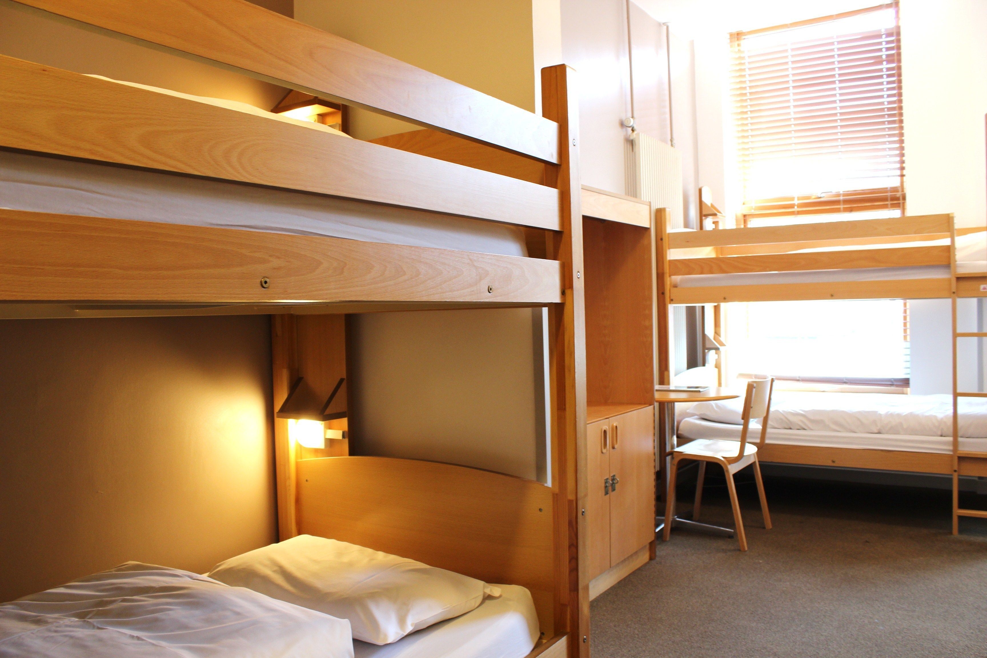 Une chambre avec un lit superposé, un bureau et une chaise, des armoires en bois et une fenêtre avec des stores.
