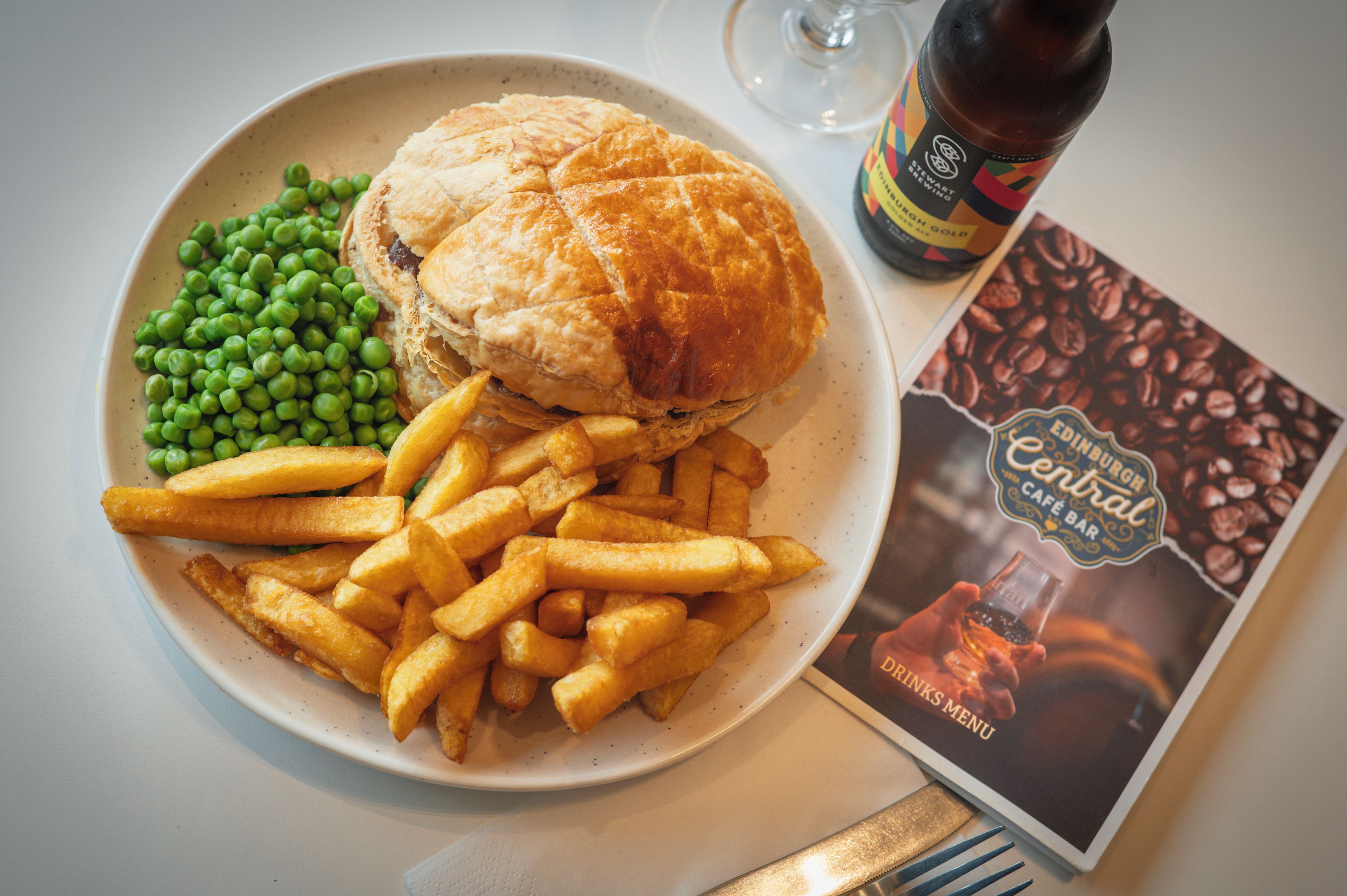 Ein Teller mit einem Sandwich, Erbsen, Pommes Frites, einer Bierflasche und einer Speisekarte.