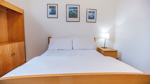 A neatly made bed with white linens, a wooden headboard, and a nightstand with a lamp. There are three framed pictures on the wall above the bed. - Edinburgh Central Youth Hostel (Edinburgh)