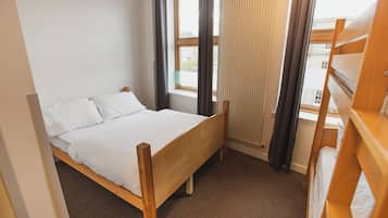A single wooden bed with white bedding in a room with a window and a radiator.