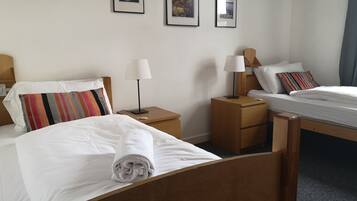 A hotel room with two beds, a wooden headboard, a nightstand with a lamp, and a small table.