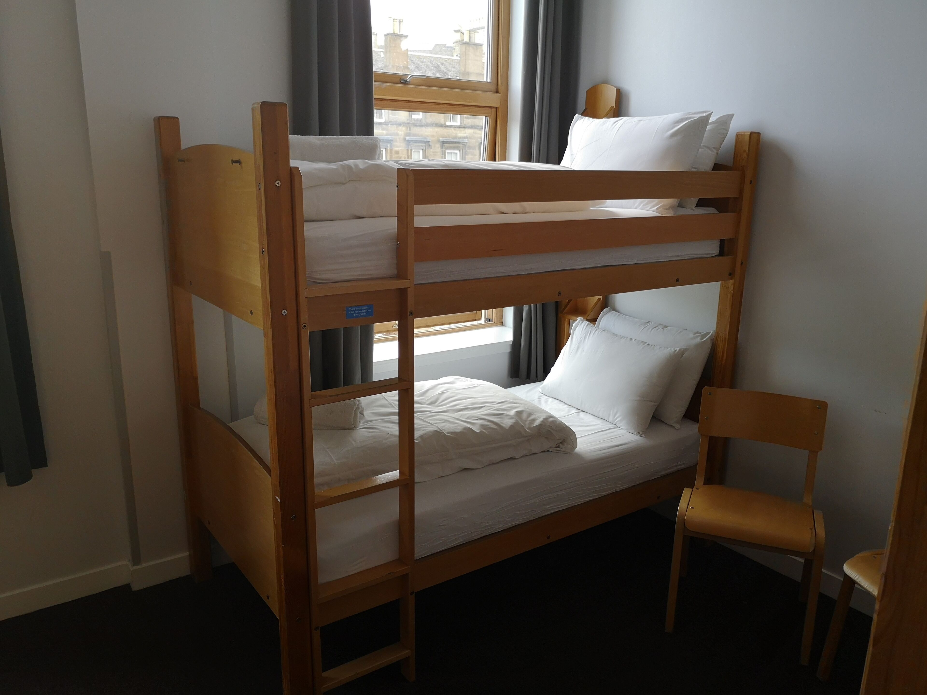 A bunk bed with a wooden frame, white bedding, and a small chair.