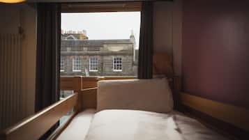 A hotel room with a bed, a window, and a view of a building outside.
