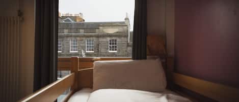 A hotel room with a bed, a window, and a view of a building outside.