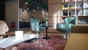 Un espace de détente moderne avec des fauteuils turquoise, une table blanche et une bibliothèque remplie de livres et d’objets décoratifs.