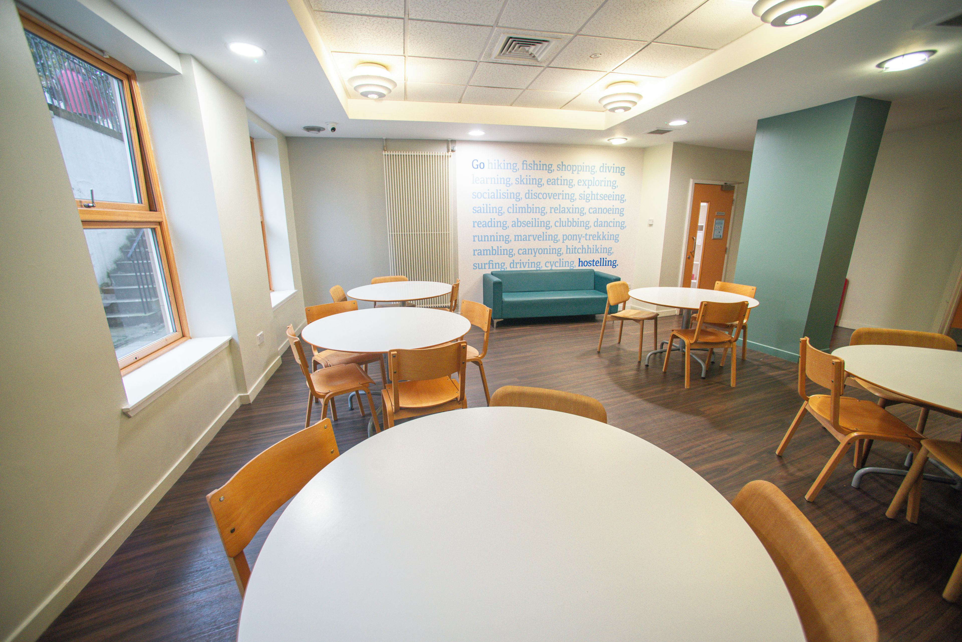 A room with round tables and chairs, a window with a view, and a wall with a list of activities.