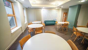 A room with round tables and chairs, a window with a view, and a wall with a list of activities.