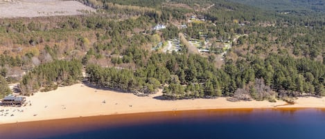 Vue aérienne d’une zone côtière avec une plage, des collines boisées et un petit bâtiment doté d’un toit.
