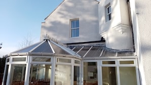 A conservatory with a glass roof and white walls, attached to a house with a gabled roof and a small window. - Cairngorm Lodge Youth Hostel (Aviemore)
