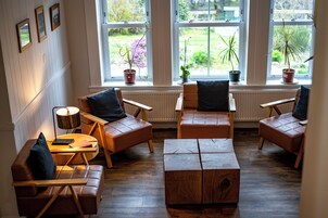 A cozy room with a fireplace, wooden furniture, and large windows with plants.