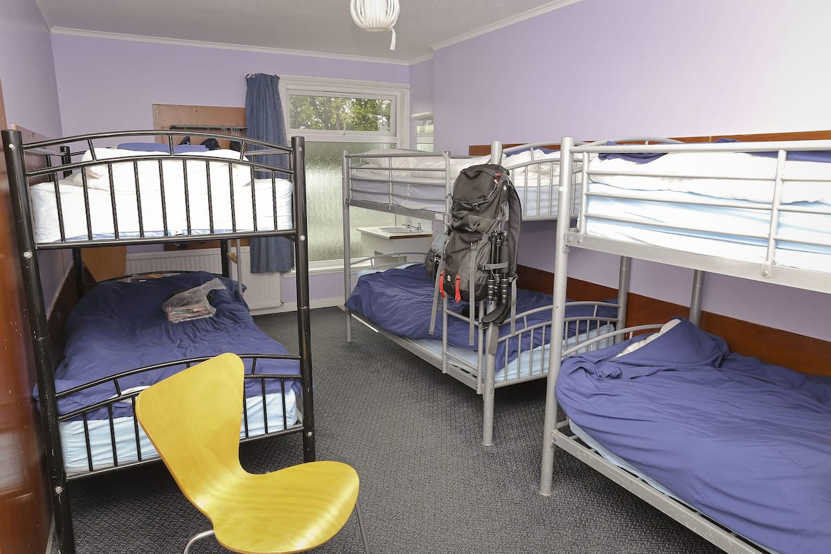 A dormitory room with bunk beds, a chair, and a window.