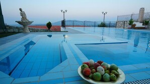 Piscina com uma estátua, uma fruteira e vista para o mar.