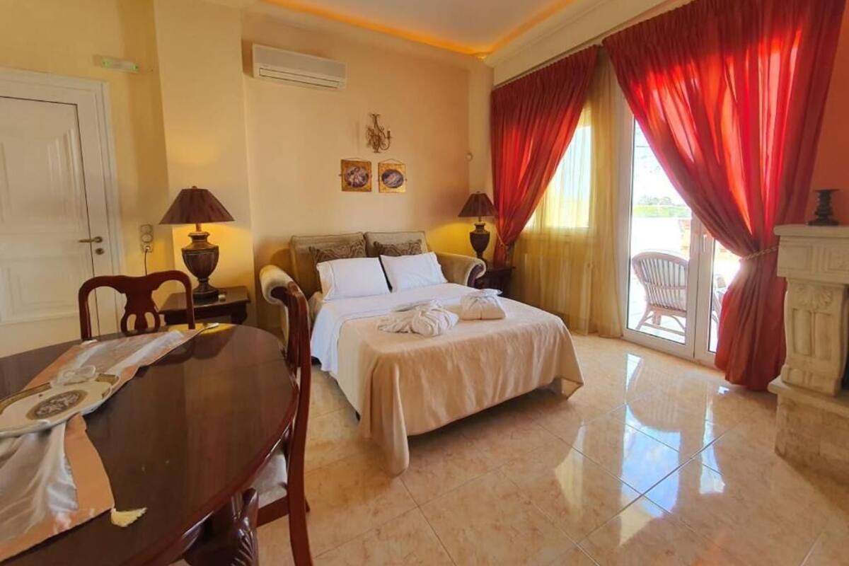 A hotel room with a bed, a dining table, chairs, a fireplace, and a view of the outdoors.