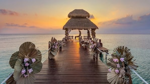 A wooden pier leading to a thatched gazebo with seating and floral arrangements. - Secrets Aura Cozumel - Adults Only - All Inclusive (Cozumel)