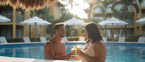 A couple by a pool with umbrellas and lounge chairs in the background.