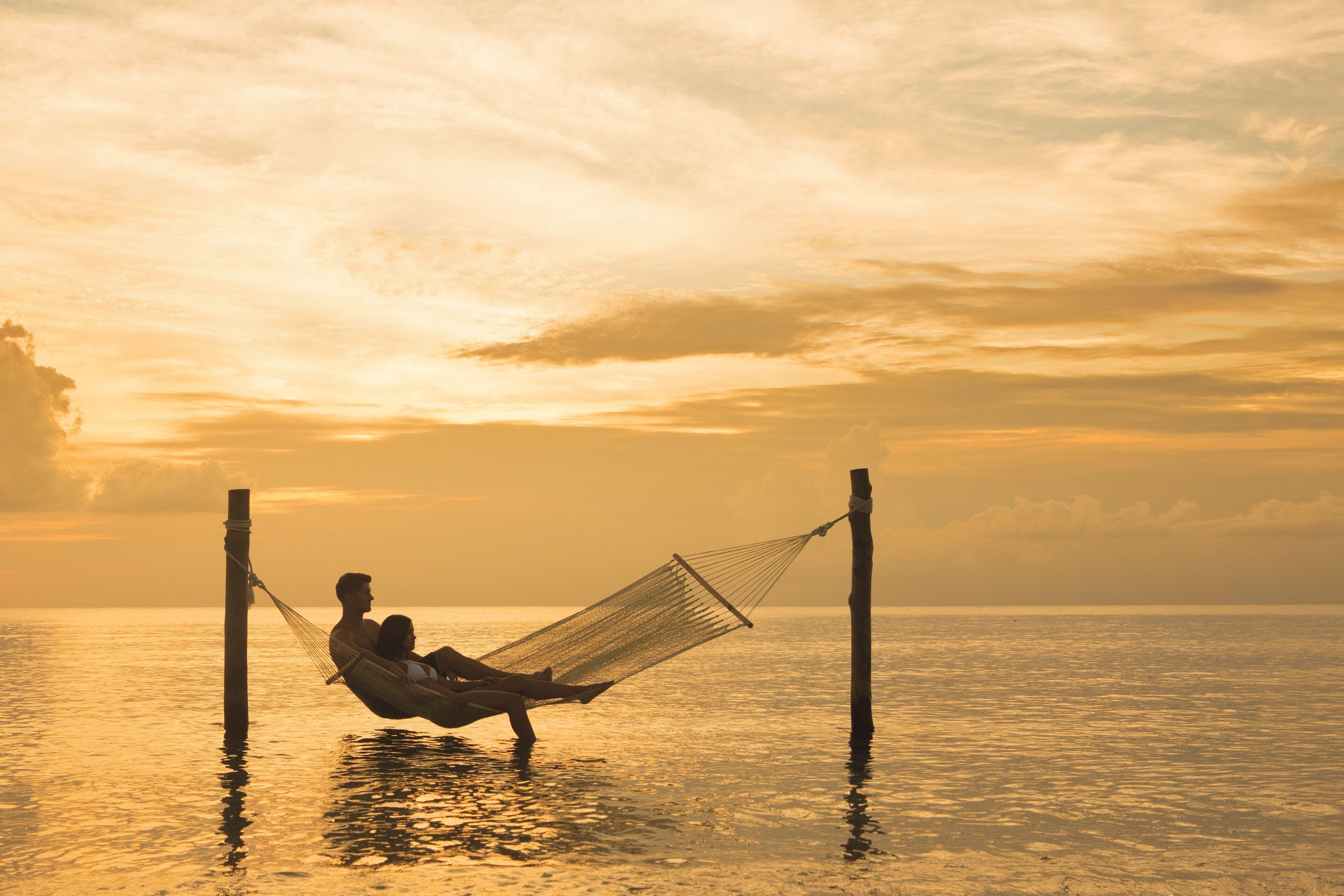 Una hamaca atada entre dos postes sobre un cuerpo de agua al atardecer.