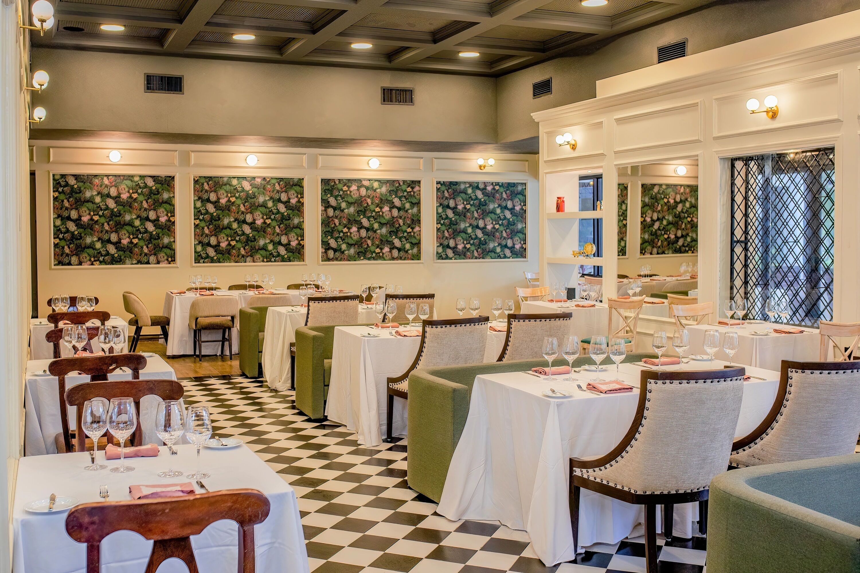 A restaurant with checkered flooring, white tablecloths, and floral wall panels.