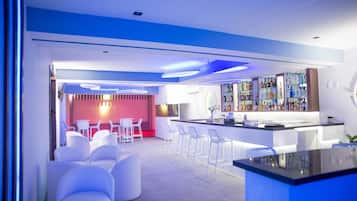 A modern bar area with white bar stools, a bar counter, and a variety of bottles.