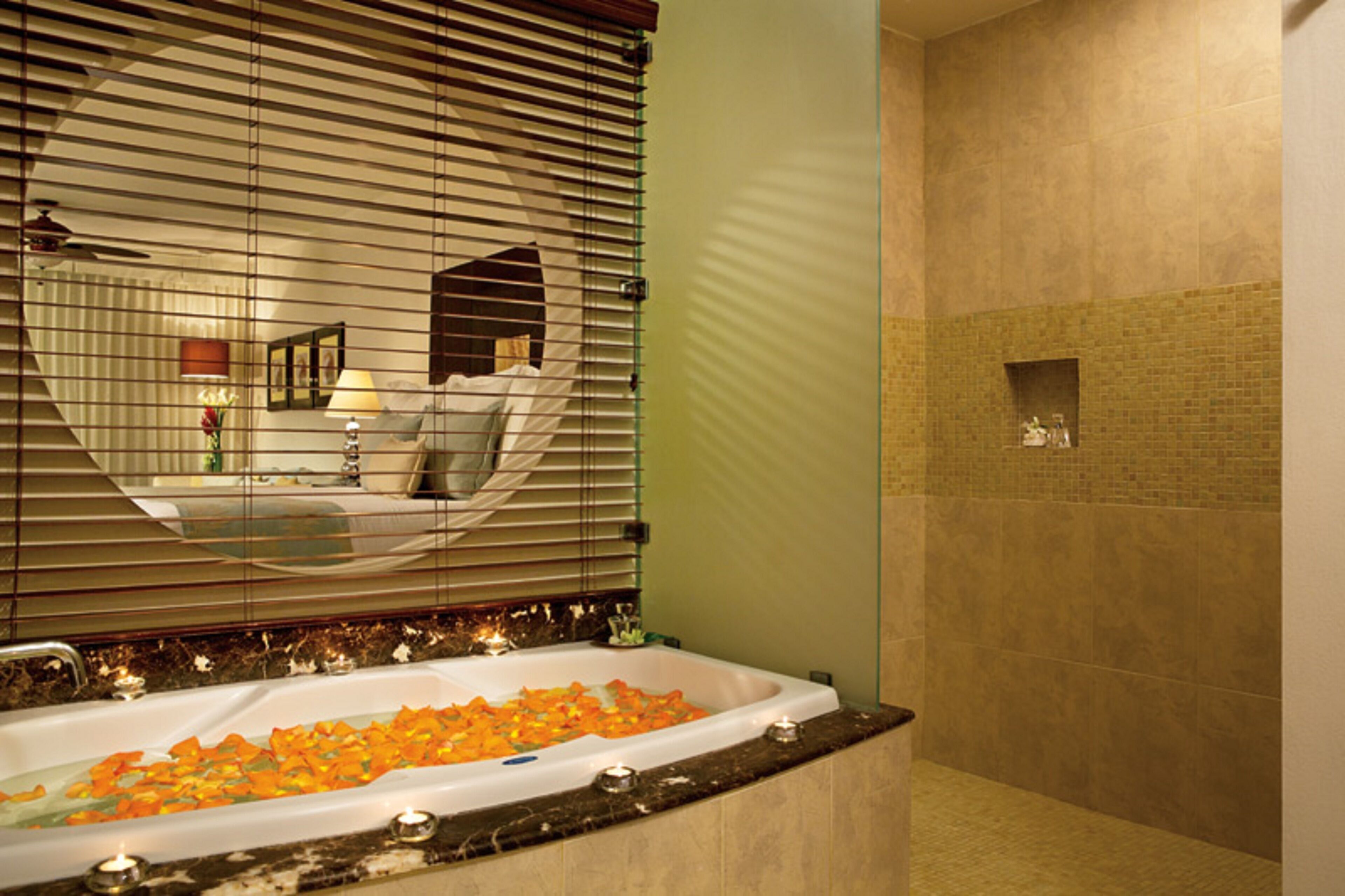 A bathroom with a large bathtub filled with rose petals, a mirror, and a green wall.