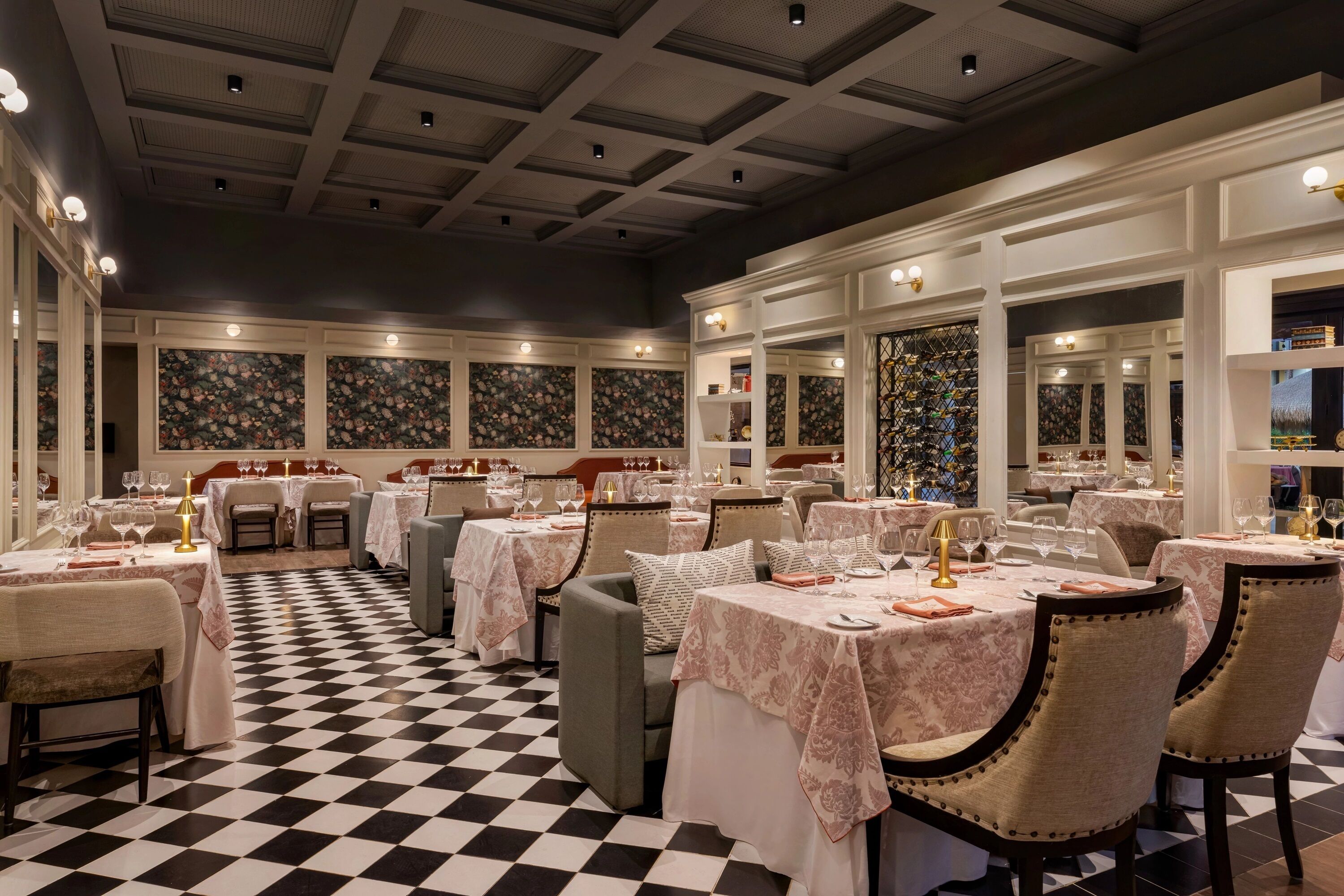 A restaurant with checkered flooring, tables set with white tablecloths, and chairs with gold detailing.