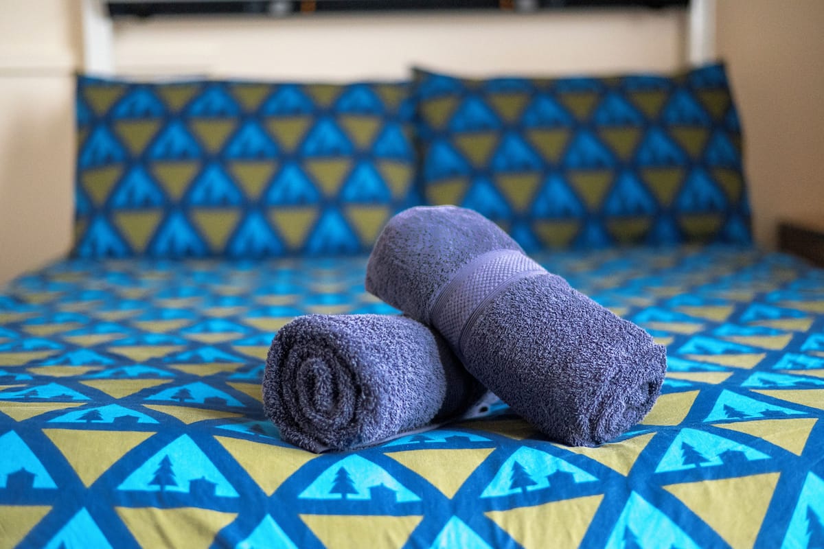 Cama com colcha azul e amarela estampada e duas toalhas enroladas.
