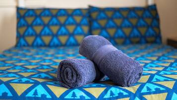Una cama con una colcha azul y amarilla estampada y dos toallas enrolladas.